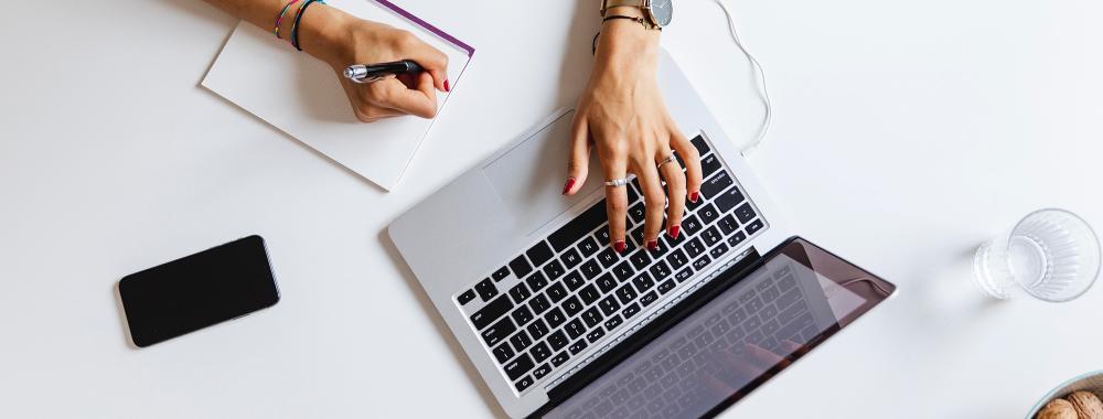 woman taking notes on an online course using a laptop