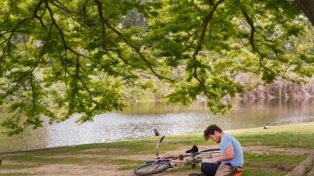 A student enjoys a sunny spring day in the Arboretum near Lake Spafford and Mrak Hall.