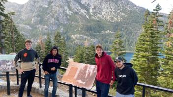 four students pose in front of a plaque at Lake Tahoe