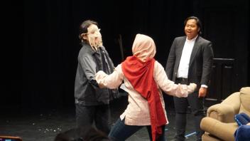 two students in costume confront each other on stage while one student watches