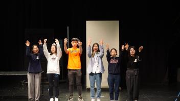 six students stand on stage with their hands in the air