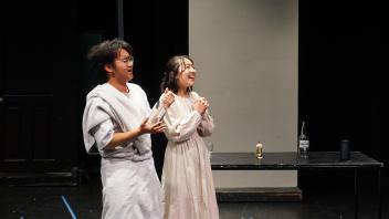 two students on stage smile while gazing off stage