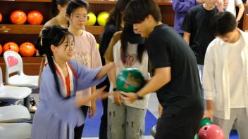 Guoyu Zhang teaches a GSP student, dressed in traditional Han Chinese attire, how to bowl at the MU Game Area.