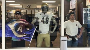 two students pose in a store window next to an Aggie football mannequin