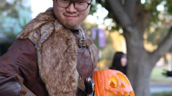 A UC Davis international student poses in costume with his carved pumpkin