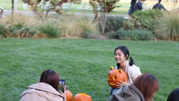 A student poses with her carved pumpkin while another student takes her photo