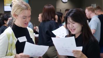 Two Global Study Program students hold a worksheet and talk aloud while engaging in an activity during orientation