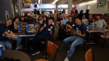Groups of Global Study Program students pose while eating a meal in food court