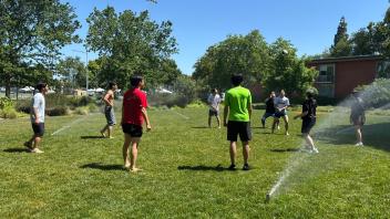 UC Davis international students play volleyball on the lawn with sprinkles on