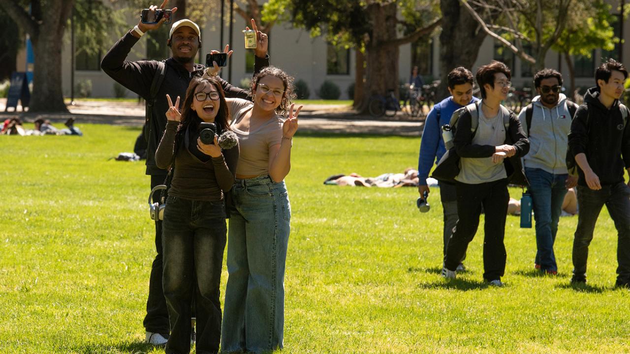 A diverse group of students show peace signs as they walk across the UC Davis Quad 