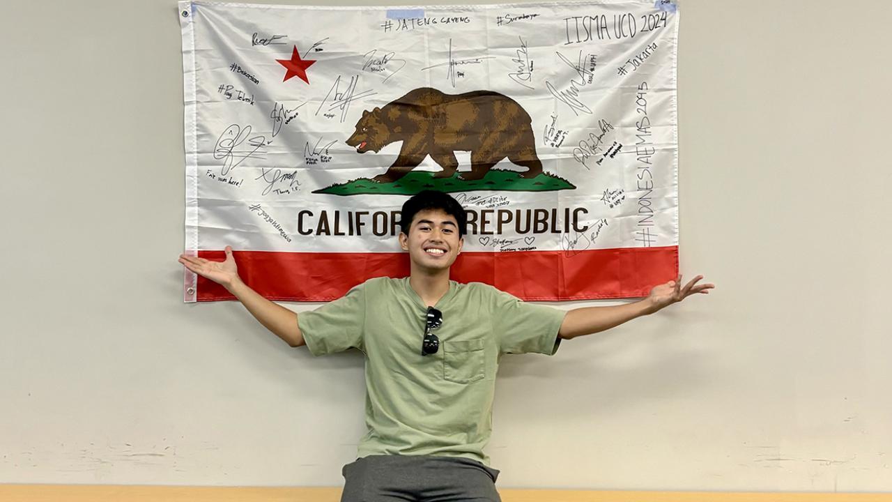 Faiz posing in front of the signed California flag during orientation