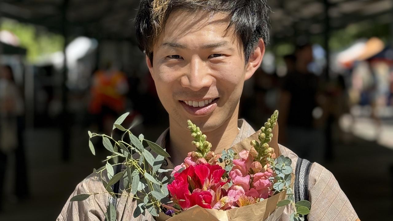 UC Davis GSP graduate Ryotaro Okada poses with flowers at the Davis Farmer's Market