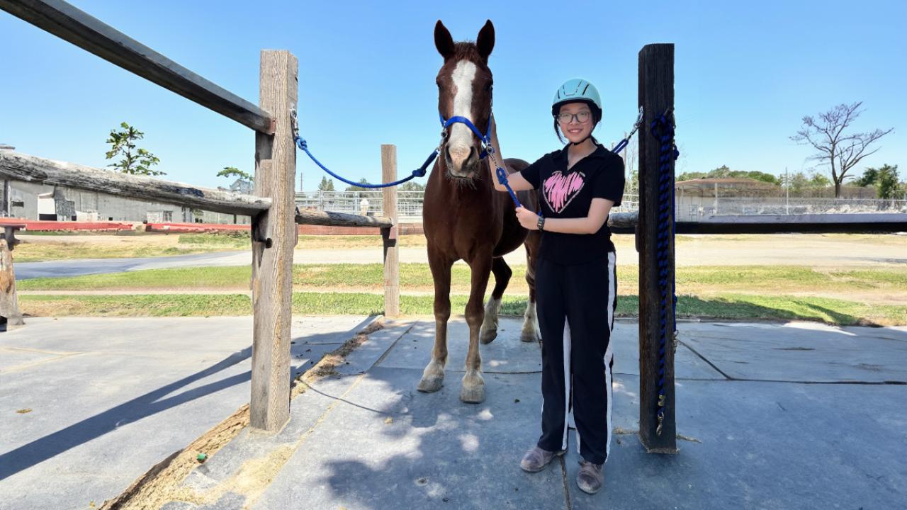 UC Davis GSP student Yizhou Liu poses with a horse during her horse riding class at the ARC