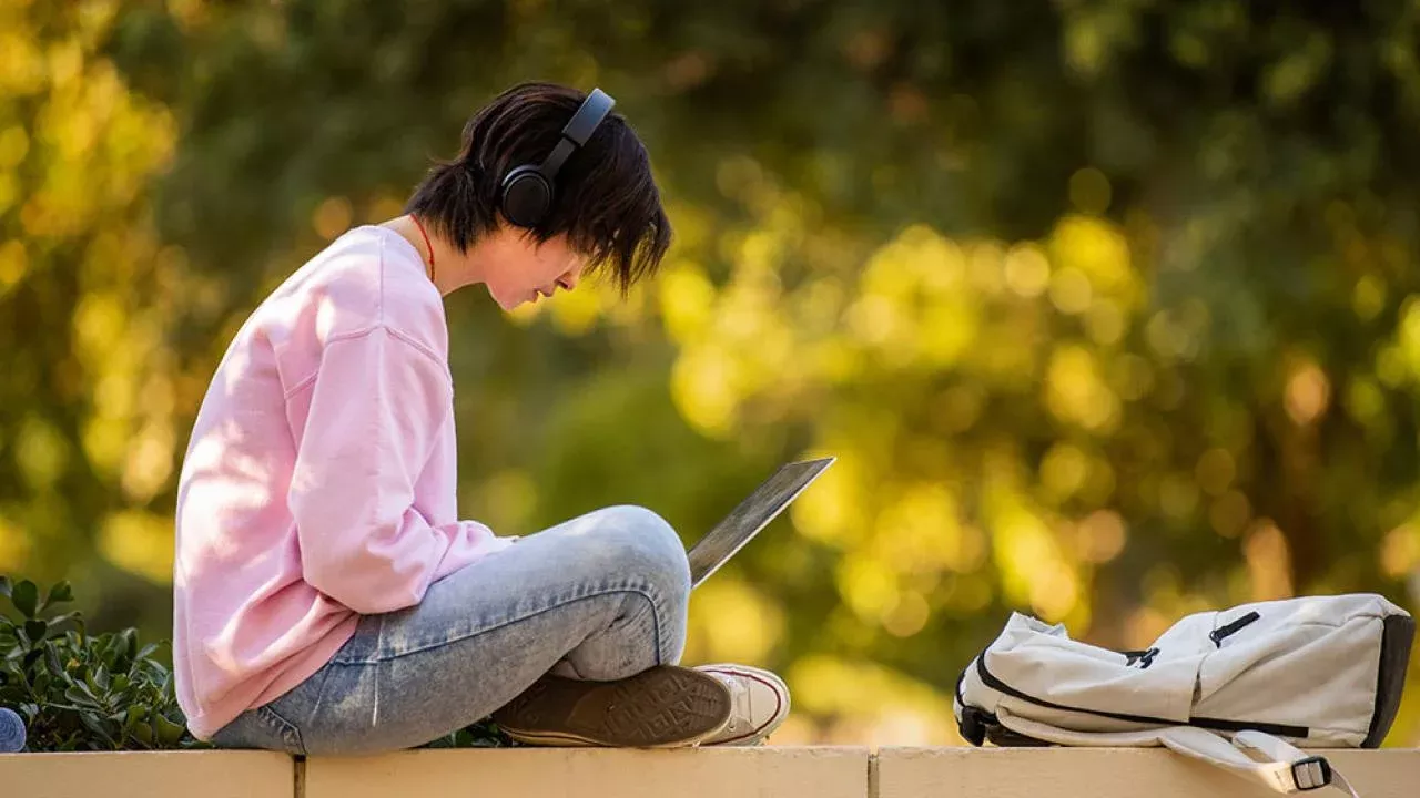 a student sits outside studying on his laptop