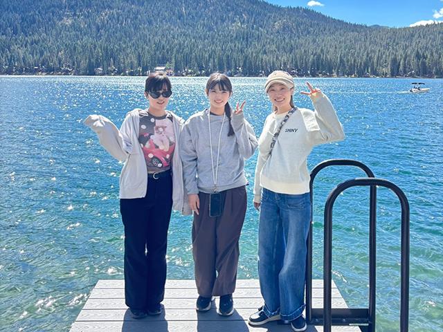 Three friends smiling on a dock by a blue mountain lake, forested shore in background
