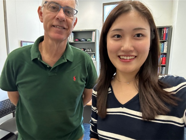 Two smiling people in an office, man in green polo and woman in navy striped top