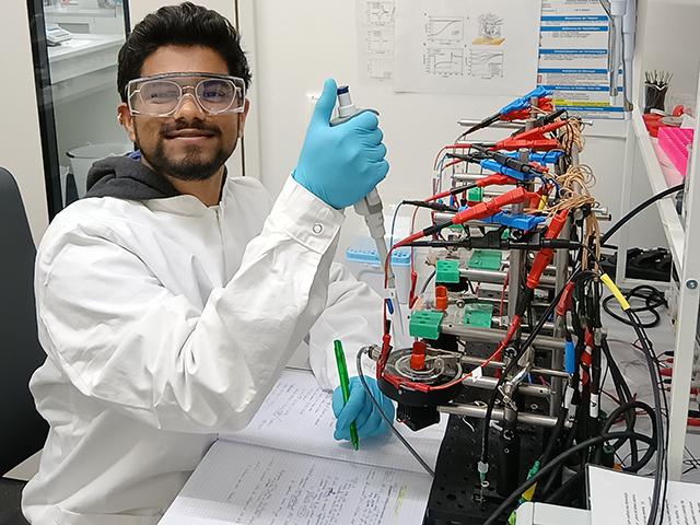 UC Davis GSP grad Nahush Modak in gloves and a lab coat conducts an experiment with lab equipment.