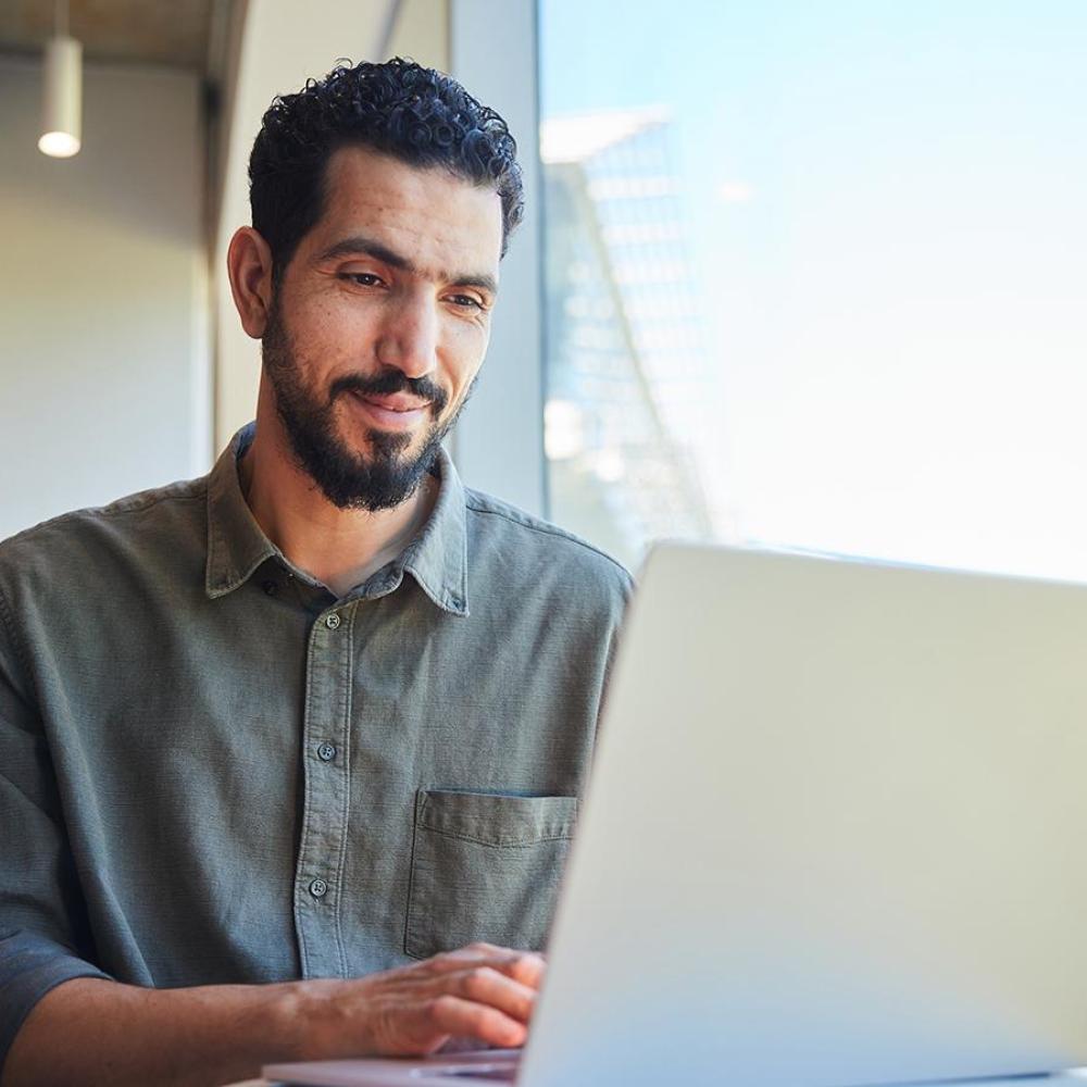 a man sits at a desk working on his laptop smiling