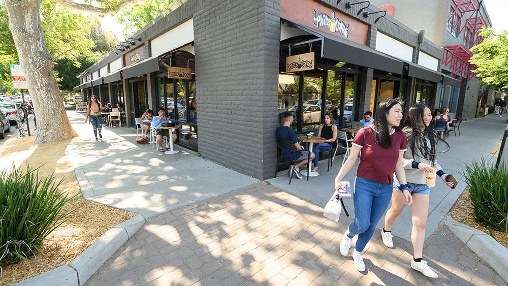 students walking in downtown Davis with people sitting at tables outside
