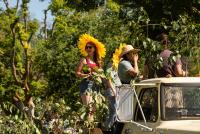 Three people on a jeep in dense jungle; woman in large yellow sunhat and another photographing