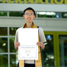 Charley Xiao stands proudly holding a certificate outside an international building.