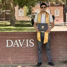 headshot of Zhankeldy Doszhanov, a Kazakh scholar who studied a UC Davis, holds his certificate of accomplishment in front of the UC Davis sign